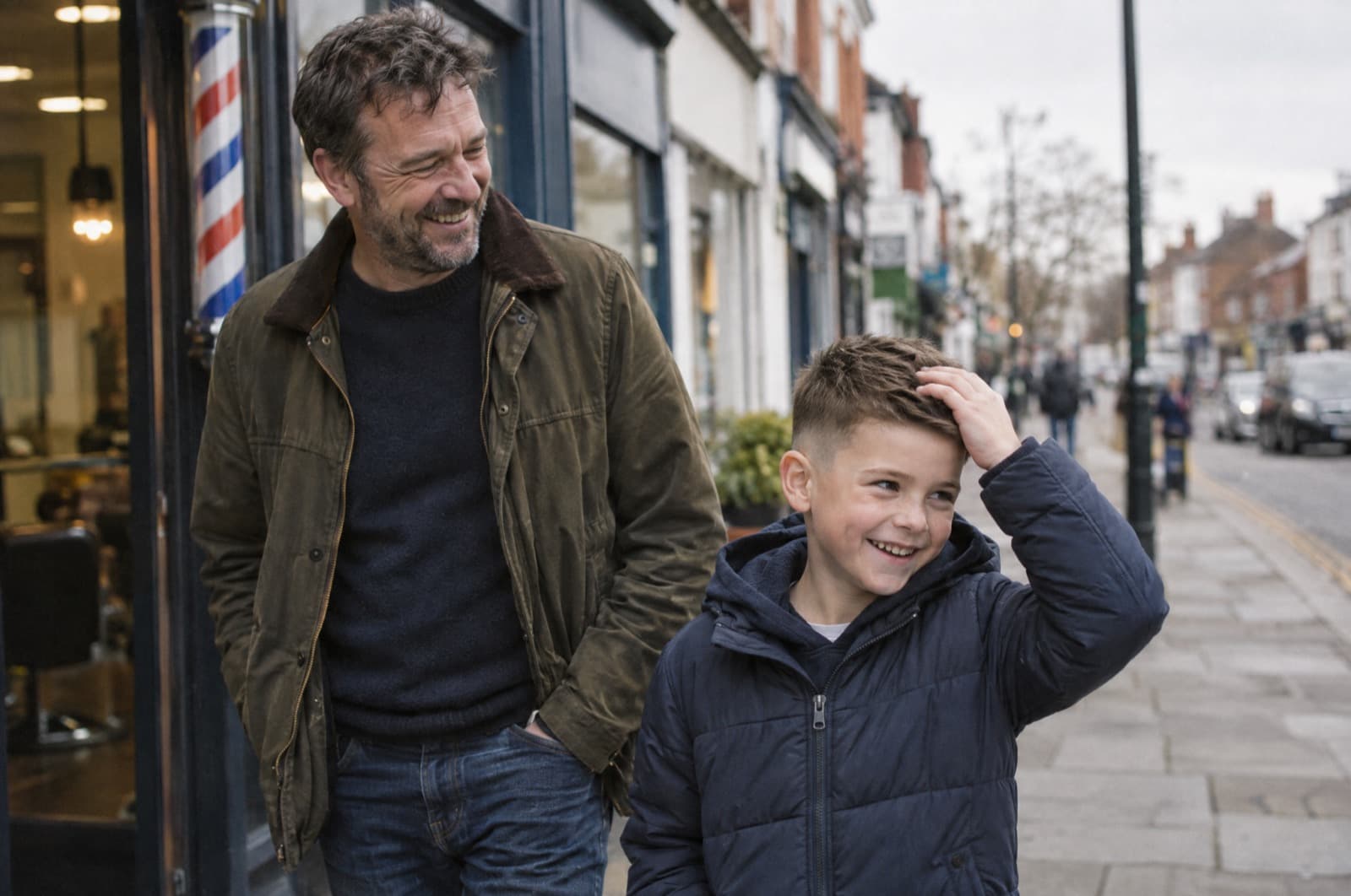 A father and his son leaving a barbershop, the boy grinning and touching his fresh haircut.