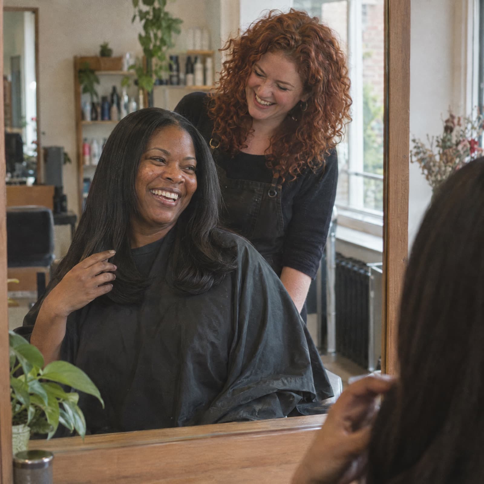 A stylist and her client laughing together at the mirror after a finished blow-dry.